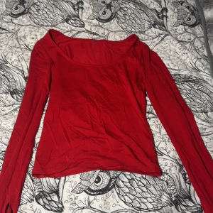 Röd långärmad topp med slits - Säljer en röd långärmad topp med rundad halsringning och slits vid ärmsluten. Toppens material känns mjukt och stretchigt, troligen bomull eller polyester. Passformen är normal och toppen är enkel men snygg, perfekt för att lyfta din outfit med lite färg.
