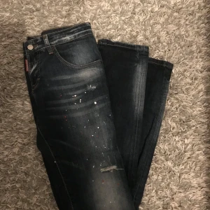 DSQUARED2 jeans - Snygga mörkblå Levis jeans med coola färgstänk och slitningar på framsidan. Klassisk femficksmodell med knapp och dragkedja. Jeansen har en rak passform och är tillverkade i robust denim. Perfekt för dig som gillar en lite edgy stil.