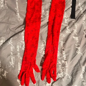 Långa röda spetsvantar - Säljer ett par riktigt snygga långa handskar i röd spets. De är transparenta med blommigt mönster och går hela vägen upp över armbågen. Perfekt om du vill sticka ut och addera lite extra edge till din outfit.