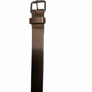 Brunt skärp i skinn med silverfärgat spänne - Snyggt och stilrent brunt bälte i skinn med klassiskt silverfärgat fyrkantigt spänne. Bältet är smalt och har en enkel design utan mönster, perfekt för att lyfta vilken outfit som helst. Passar dig som gillar minimalistisk och tidlös stil.