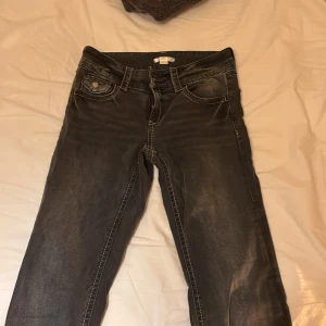 Svarta jeans från Gina Tricot, stl 170 - Snygga svarta jeans från Gina Tricot i storlek 170. Jeansen har klassisk femficksdesign, markerade sömmar och en lätt tvättad look. Perfekta för dig som gillar en enkel men stilren vibe. Materialet är jeans och färgen är mörkgrå till svart.