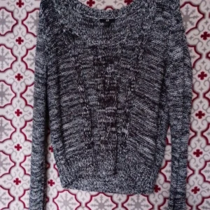 Gråmelerad stickad tröja - Säljer en gråmelerad stickad tröja med snyggt kabelmönster framtill. Tröjan har rund hals och långa ärmar, samt ribbade muddar vid ärmslut och nederkant. Perfekt för dig som gillar en chill och klassisk look.