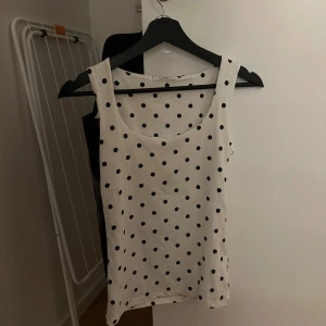 Vit prickig linnetopp från Zara - Säljer en vit linnetopp från Zara med svarta prickar. Toppen är ärmlös och har en rundad halsringning. Materialet är mjukt och lätt, perfekt för varma dagar. Prickmönstret ger en lekfull och trendig vibe. Storlek S enligt etiketten.