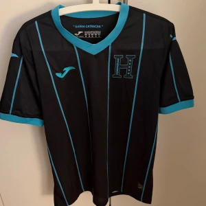 Svart/blå Honduras fotbollströja  - Snygg svart/blå Honduras fotbollströja i storlek M. Endast andvänd 1 gång innan, så gott som ny! Perfekt och ha när man kanske ska iväg och träna eller likande tillfällen.😊 hör av er vid frågor och pris kan diskuteras 