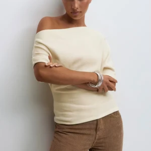 Offshoulder crämfärgad stickad topp - Säljer en superfin offshoulder topp i crämfärg. Toppen är stickad och har en snygg, asymmetrisk halsringning som visar ena axeln. Passformen är normal och materialet känns mjukt mot huden. Perfekt att styla med jeans eller kjol för en trendig look.
