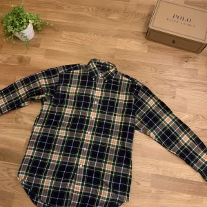 Rutig skjorta från Ralph Lauren M - Riktigt snygg rutig skjorta från Ralph Lauren i storlek M. Skjortan har klassisk button-down krage, långa ärmar och knappar framtill. Färgerna är mörkblå, grön, gul, vit och röd. Materialet är 100% bomull och den har den ikoniska broderade loggan på bröstet.