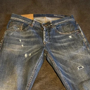 Dondup jeans blå, storlek 30 - Säljer ett par Replay Grover jeans i blå tvätt med slitna detaljer och trasiga partier för en cool, edgy look. Klassisk femficksmodell med orange sömmar och raka ben. Materialet är robust denim som sitter snyggt och bekvämt.