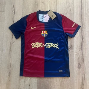 Barcelona fotbollströja Nike S - Säljer en officiell FC Barcelona fotbollströja från Nike i storlek S. Tröjan har klassisk halva röd och halva marinblå design, korta ärmar och guldfärgade detaljer som logga och tryck. Materialet är lätt och andas, Dri-Fit polyester. Perfekt för dig som älskar Barca!