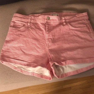Randiga rosa shorts med fickor - Snygga rosa och vita shorts med smala ränder, klassisk femficksmodell och knappstängning fram. De har bälteshällor och är tillverkade i ett mjukt bomullstyg som känns skönt mot huden. Perfekta för varma dagar och en chill stil.