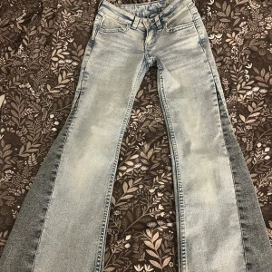 Ljusblå bootcut jeans från H&M Divided - Säljer ett par ljusblå bootcut jeans från H&M Divided. Jeansen har snygg tvättad look, vida ben och coola fickor med lock och knapp bak. Perfekta för dig som gillar retrovibbar och vill sticka ut lite extra.