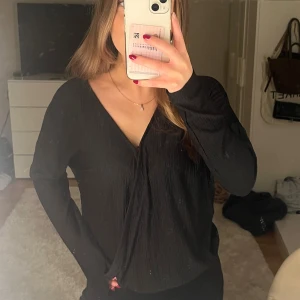 Svart omlott blus - Svart blus med omlott-design och v-ringad hals från Lindex. Blusen har långärmade ärmar och är gjord i ett lätt, krinklat tyg med struktur. Blusen är endast använd fåtal gånger och är i mycket bra skick. 💕