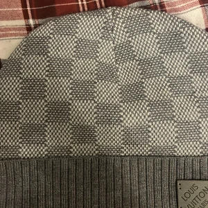 Grå rutig mössa - Snygg grå mössa med klassiskt rutigt mönster och ribbad kant. Märkesplakett framtill. Perfekt accessoar för att hålla stilen kallare dagar.