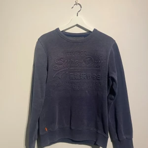 Superdry blå tröja, storlek S - Blå Superdry tröja med tryck framtill. Tröjan har en rund halsringning och muddar vid ärmslut och nederkant. En stilren och bekväm tröja som passar perfekt till vardags. Riktigt fet look.  Skick: Gott skick, sparsamt använd utan defekter.  Storlek: S (normal i storleken).  Kolla gärna in mina andra annonser.   Skriv vid frågor eller ifall du vill ha fler bilder. 