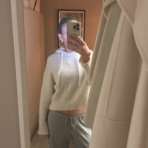 Vit croppad hoodie med huva - Mysig vit croppad hoodie med huva och snörning. Tröjan har lång ärm och är tillverkad i ett fluffigt stickat material som känns supergosigt. Perfekt för chill dagar och när du vill ha något bekvämt men ändå snyggt.