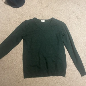 Mörkgrön v-ringad tröja från Vila - Mysig mörkgrön stickad tröja från Vila med v-ringning och långa ärmar. Perfekt för lager-på-lager och passar till både jeans och kjol. Ribbstickade muddar vid ärmslut och nederkant ger en snygg finish.