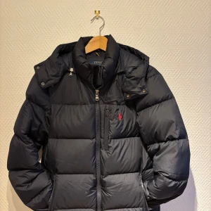 Mörkblå pufferjacka från Ralph Lauren - Skön och varm vinterjacka från RL. Ser lite svartare ut på bild än verkligeheten men skriv gärna för fler bilder, pris kan disskuteras vid smidig affär. Varsamt använd så inga deffekter förekommer.