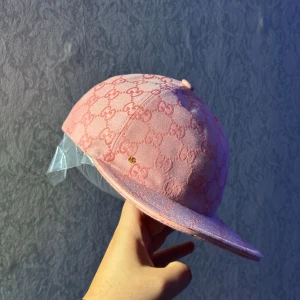 Rosa Gucci keps med GG-mönster - Snygg rosa keps från Gucci med det klassiska GG-mönstret över hela kepsen. Kepsen har böjd skärm och justerbar rem baktill. Tillverkad i bomull och har märkets logga på insidan. Perfekt för dig som vill sticka ut med en lyxig streetstyle.