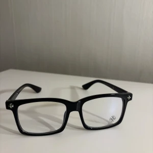  Chrome Hearts glasögon Anti blue light - Snygga svarta glasögon från Chrome Hearts med rektangulär form och coola silverdetaljer på bågarna. På glaset finns en diskret blomdekor och på sidorna syns märkets logga i silver. Perfekt accessoar för dig som vill sticka ut med stil.