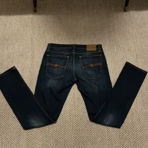 Mörkblå Nudie Jeans 30/32 - Snygga mörkblå Nudie Jeans med klassisk orange söm på bakfickorna och läderpatch i midjan. Modellen har smal passform och raka ben, tillverkade i mjukt jeansmaterial. Perfekt för dig som gillar stilrena och moderna jeans. Riktigt sköna och perfekt om du gillar att lyxa till det. Bra skick och storleken är 30/32! Hör av dig gällande frågor och priset kan diskuteras. Finns även någon enstaka slitning