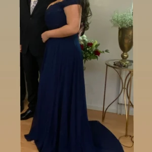 Marinblå långklänning med spets dressroom  - Säljer en marinblå långklänning med vacker spets upptill och offshoulder-ärmar. Klänningen har en böljande kjol i lätt material och en elegant v-ringad urringning. Perfekt för bal eller fest. Kjolen har extra längd baktill för en dramatisk look.