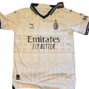 AC Milan vit matchtröja Puma - AC Milan fotbollströja från Puma i vit med subtilt grafiskt mönster och svarta detaljer på krage och ärmslut. Tryckta loggor för Emirates och Wefox, samt ACM-emblem på bröstet. Tillverkad i lätt och ventilerande polyester, perfekt för match eller träning.