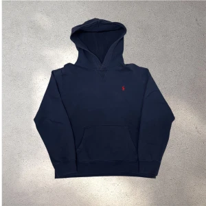 Mörkblå hoodie från Polo Ralph Lauren - Snygg mörkblå hoodie från Polo Ralph Lauren med klassisk röd logobrodyr på bröstet. Tröjan är något urtvättad och är lite sliten vi ärmmudden. Skickar snabbt efter att du har beställt✅📦 storlek xl 18-20 är samma som S i herrstorlek.