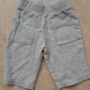Shorts - Säljer ett par grå shorts i mjukt bomullsmaterial med bred resår i midjan och två stora fickor framtill. De har en enkel och clean look, perfekt för chill dagar. Passformen är normal och färgen är ljusgrå.