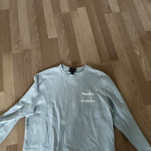 Ljusblå långärmad tröja H&M - Snygg ljusblå långärmad tröja från H&M med trycket 'Studio Archive' på bröstet. Tröjan har rund hals och är gjord i mjuk bomull, perfekt för chill dagar. Enkel och stilren design som funkar till jeans eller mjukisbyxor.