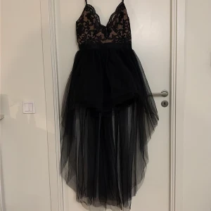 Svart långklänning med spets från Goddiva - Supersnygg svart långklänning från Goddiva med transparent mesh och spetsdetaljer upptill. Klänningen har axelband, v-ringad urringning och en voluminös kjol i lager av tunn tyll som ger en dramatisk look. Endast använd en gång. Priset går att diskuteras!