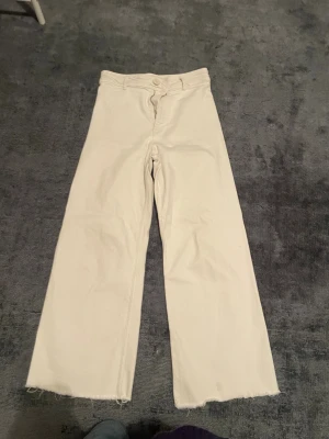 Zara vita straight jeans Marine - Säljer ett par vita raka jeans från Zara, modell The Marine Straight. Byxorna har råa, fransiga benslut och klassiska bakfickor. De är tillverkade i bomull och har en snygg, enkel look som passar till allt.