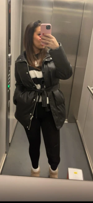 Svart pufferjacka  - Säljer en svart pufferjacka från med snyggt bälte i midjan. Jackan har lång ärm, hög krage och både dragkedja och knappar framtill.