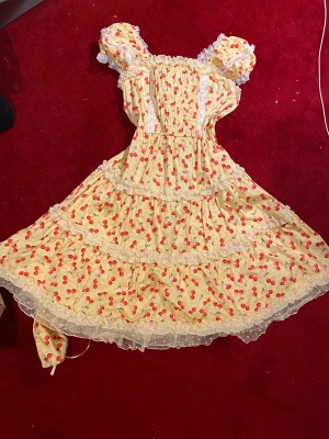 gul lolita klänning - supersöt gul lolita klänning från Bodyline med röda körsbär, puffärmar och spetsdetaljer. skärp, korsettknytning i ryggen och  dekorerad med vita spetsar. 