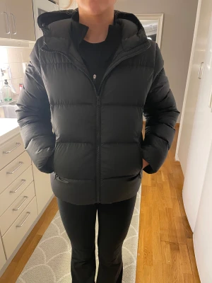 Svart pufferjacka från Colmar - Säljer en svart pufferjacka från Colmar med huva och dragkedja framtill. Jackan har en clean look, diskret logga på ärmen och är riktigt fluffig. Perfekt för kalla dagar när du vill hålla värmen och ändå se snygg ut.