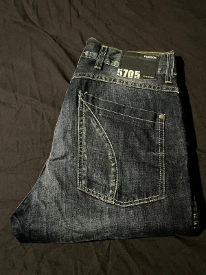 Mörkblå jeans från Pearson W32 L32 - Snygga mörkblå jeans från Pearson, modell 5705. De har coola slitningar och kontrastsömmar i gult, klassisk femficksdesign och raka ben. Jeansen är tillverkade i slitstarkt denim och har en normal passform som funkar till de flesta stilar. Hör av er vid frågor!