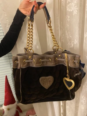 Juicy Couture axelväska med hjärtdetalj - Säljer en jätte snygg brun axelväska från Juicy Couture för den kommer inte längre till andvänding, den är i brun samett och har guldigt ditaljer💕pris kan diskuteras!🌸🌸