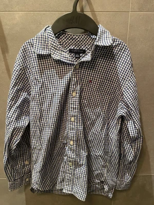 Blårutig skjorta Tommy Hilfiger M - Snygg blårutig skjorta från Tommy Hilfiger i storlek M. Skjortan har klassisk krage, långa ärmar och knappar framtill. Tillverkad i mjuk bomull med ikonisk Hilfiger-logga broderad på bröstet. Perfekt för dig som gillar stilrena och tidlösa mönster.