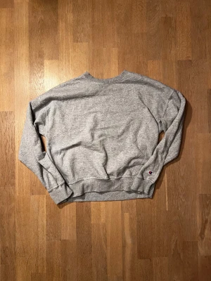 Grå sweatshirt från Champion - Grå sweatshirt från Champion med broderad logga på bröstet och ärmen. Klassisk rund hals och ribbade muddar vid ärmslut och nederkant. Perfekt för chill dagar och enkel att matcha med jeans eller joggers. Den är S men taggen är tyvärr borta.  Skick 7/10 behöver sig en tvätt ✅ Skickar inom 48 timmar om inte samma dag 🚚