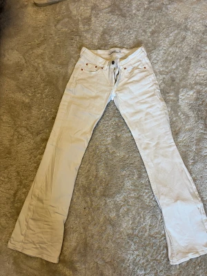 Vita bootcut jeans från Junkyard - Säljer ett par vita jeans från Junkyard med klassisk femficksdesign och snygg bootcut-passform. Byxorna har låg midja och är tillverkade i mjukt bomullsmaterial med en lätt stretch. Perfekta för dig som gillar en clean och fräsch look.