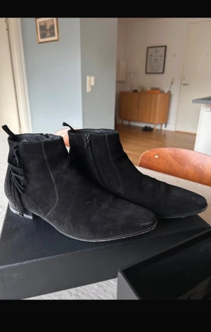 Saint Laurent boots - Säljer ett par svarta boots från Saint Laurent i mjuk mocka med spetsig tå och låg klack. Skorna har snygga fransdetaljer på sidan och dragkedja på insidan för enkel påtagning. Perfekt för dig som gillar stilrena och exklusiva skor med lite edge.