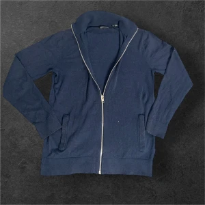 Marinblå kofta från Jack & Jones - Marinblå kofta från Jack & Jones 👔 med hel dragkedja framtill ⚡ och ribbade muddar ✨. Tröjan har två praktiska fickor 👜 och är långärmad med mjukt material som känns skönt mot huden 🧵. Perfekt för dig som gillar enkel och stilren design 😎.  ⚠️ Litet hål baktill, men inget som märks! 📦 Skickar paket snabbt – samma dag som beställning! ⭐ Nöjda kunder som tidigare kan intyga! 💬 DM vid frågor!