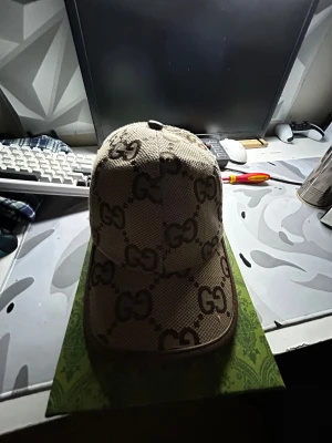 GG keps - Säljer en beige keps från GG med det klassiska GG-mönstret i brunt över hela kepsen. Justerbar rem bak i brunt skinn med GG-logga. Kepsen har böjd skärm och är tillverkad i ett grovt, slitstarkt tyg som ger en lyxig vibe.