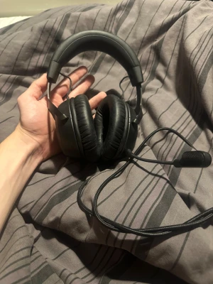 HyperX Cloud II Gaming Headset - HyperX Cloud II gamingheadset med kabel och mikrofon. Over-ear design med mjuka kuddar för komfort under långa spelsessioner. Headsetet ser ut att vara i gott skick utan synligt slitage eller defekter. Perfekt för gaming och kommunikation.