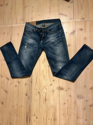 Mörkblå jeans från dondup med slitningar - Snygga mörkblå jeans från dondup med slitna detaljer och lätt tvättad look. Klassisk femficksmodell med knappgylf och kontrastsömmar. Jeansen har en rak passform och är tillverkade i robust denim för en cool vardagsstil.