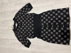 Svart mönstrad kjol med topp från Lindex  -  svart kortkjol med topp från Holly & White med beige gö mönster och guldknappar framtill. Setet är stickat och har en elastisk midja som gör den bekväm och enkel att bära. 