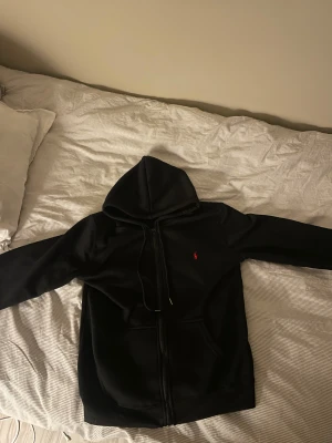 Svart hoodie från Polo Ralph Lauren - Svart hoodie från Polo Ralph Lauren med rött broderat logotyp på bröstet. Tröjan är aldrig använd. Nytt skick på tröjan.Bra kvalité.