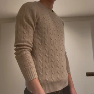 Beige kabelstickad kashmirtröja Soft Goat - Säljer en beige kabelstickad tröja från Soft Goat i 100% kashmir. Tröjan har rund halsringning, ribbade muddar och lång ärm. Perfekt för dig som gillar en klassisk och clean look med extra lyxig känsla.