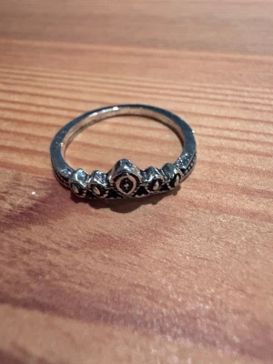 Silverfärgad tiararing med pärldetaljer - Snygg ring i silverfärg med tiaraformad design och små pärlliknande detaljer längs ovansidan. Perfekt för dig som gillar unika och lite kungliga smycken. Ringen har fina detaljer och passar dig som vill sticka ut med din stil.