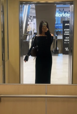 Svart lång offshoulder klänning, lite genomskinlig  - Snygg svart långklänning med offshoulder-design och långa ärmar. Klänningen har en figurnära passform som framhäver siluetten och ger en elegant look. Perfekt för dig som gillar stilrena och minimalistiska plagg med en modern touch.