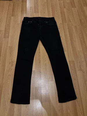 Svarta jeans från Nudie Jeans Co 34/32 - Säljer ett par svarta jeans från Nudie Jeans Co i storlek 34/32. Klassisk femficksmodell med raka ben och normal passform. Jeansen är tillverkade i ett slitstarkt denimtyg och har subtila detaljer som svarta sömmar och knappgylf.