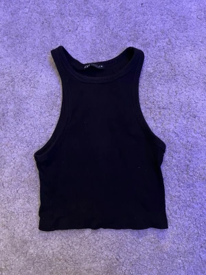 Svart ribbad linnetopp från Zara - Säljer en svart croppad linnetopp från Zara i storlek S. Toppen har en hög halsringning och är ärmlös med ribbad struktur. Perfekt för dig som gillar en enkel och stilren look. Materialet är mjukt och stretchigt för skön passform.